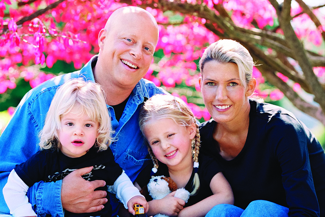 A smiling man and woman holding their two young daughters 