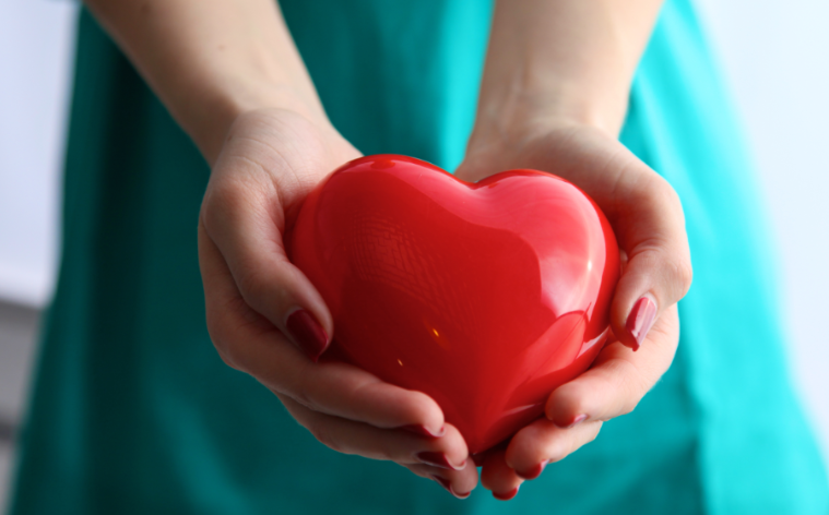 Hands with long red nails cupping a plastic red heart