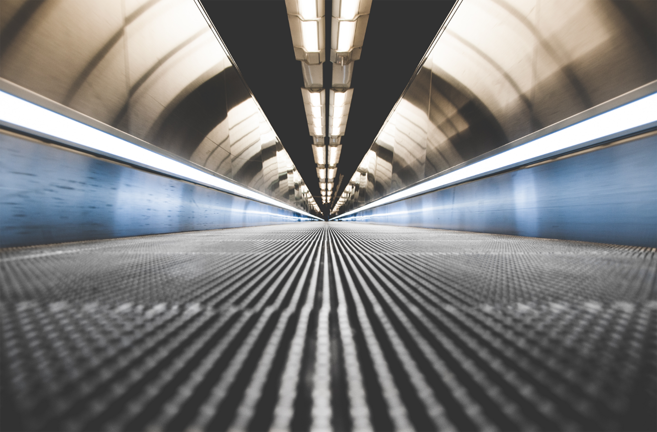 Ground-level view of a metal and glass walkway with a human figure off in the far distance